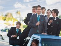 Teenage boys in suits smiling from car
