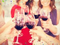 group of women holding up wine glasses with red wine in them.